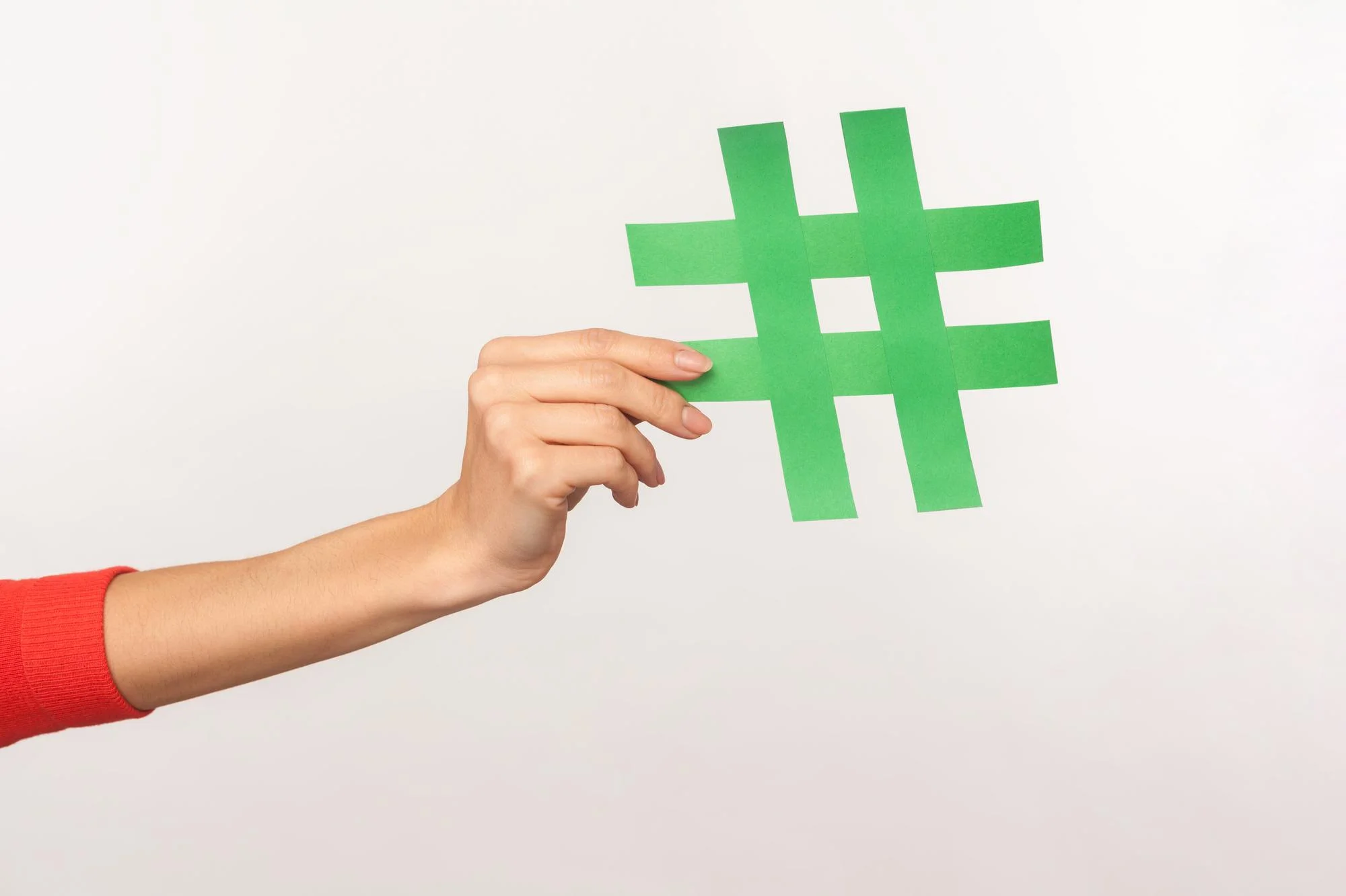 Photo follow trend, join popular blog. closeup of female hand holding green hashtag sign, sharing tagged message, recommending viral content, meme or post. indoor studio shot isolated on white background
